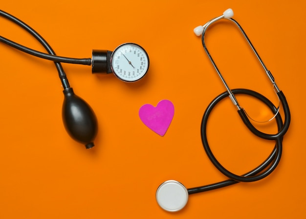 Medical monometer, stethoscope, decorative heart on orange background