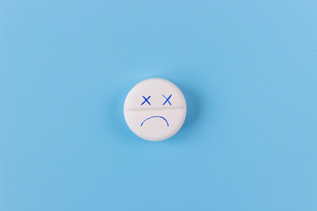 Medical pill in the form of a dead emoticon on a blue background. Health care, medicine, treatment, therapy concept.