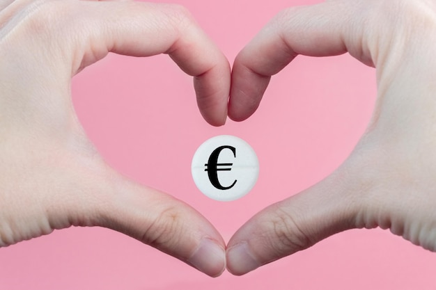 Medical pill with a euro currency sign inside a heart made from hands on a pink background The concept of a rise in price of medicines in Europe Expensive treatment