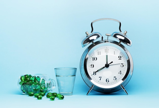 Medical pills glass water and metal alarm clock on a blue background concept medicine and treatment