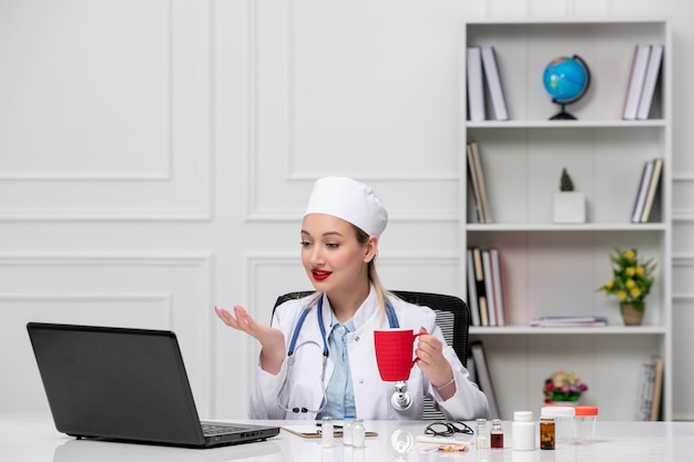 Medical pretty cute doctor in white lab coat and hat with computer with red cup