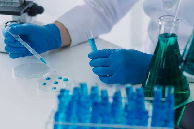 Medical or scientific researcher researching and experimenting Multicolored solution vial and microscope In the laboratory or in the laboratory by wearing blue gloves and white clothing completely