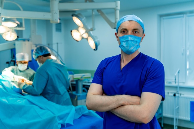 Medical specialist in modern operating room stands cross hands in surgery room Doctors perform a surgery on background with modern equipment Closeup