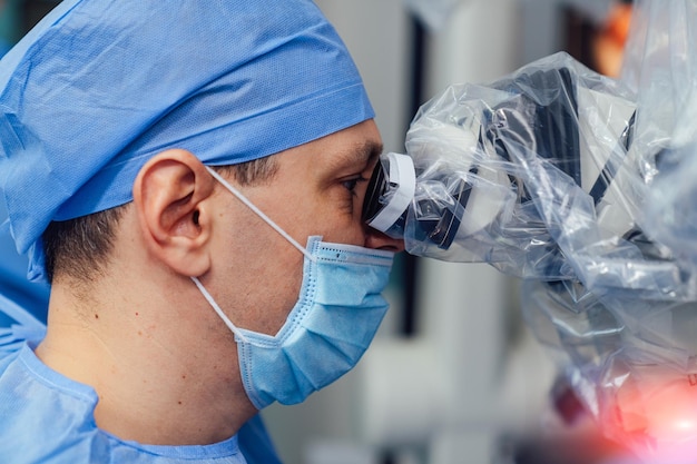 Medical specialist performing surgery using modern equipment Profile of surgeon in mask looking into microscope in the operating room