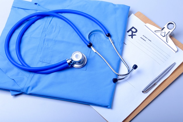 Medical stethoscope lying on patient medical history list, RX prescription and blue doctor uniform closeup.