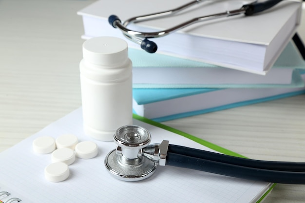 Medical stethoscope with books and tablet on wooden table