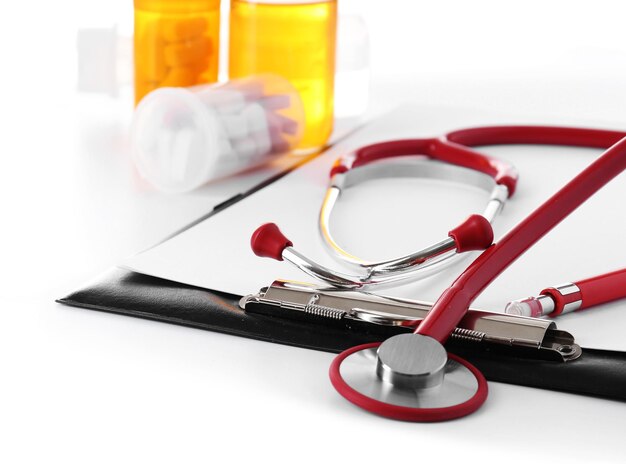 Medical stethoscope with clipboard and pills isolated on white