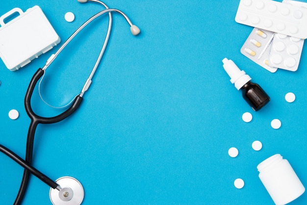 Medical stethoscope with pills on blue background.