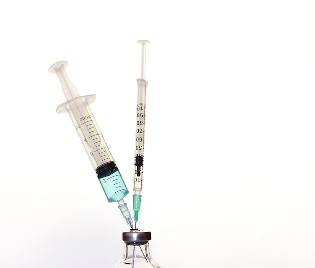 A medical syringe and a bottle of vaccination on a light background.