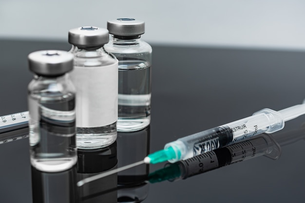 Medical treatment syringes and vaccine bottles in reflecting dark table