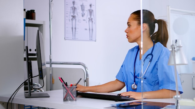 Medical woman nurse typing on computer patient health report, sitting in hospital office. Healthcare physician in medicine uniform writing treatments making appointments checking registration.