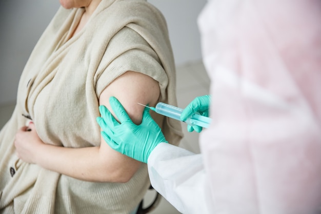 A medical worker in green gloves gives a woman a covid 19 shot in the shoulder