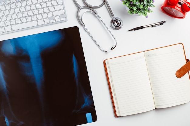 Medical workplace with stethoscope,notebook,pen,keyboard and x-ray film on withe desk.Top view