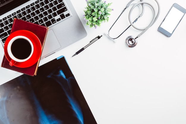 Medical workplace with stethoscope,pen,laptop,smart phone and x-ray film on white desk.Top