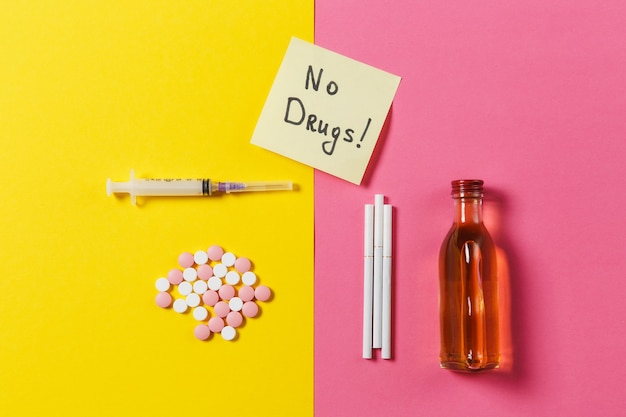 Medication colorful tablets pills abstract empty syringe needle, bottle alcohol cigarettes on yellow pink rose background