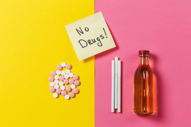 Medication colorful tablets pills arranged abstract, bottle alcohol, cigarettes on yellow pink rose background