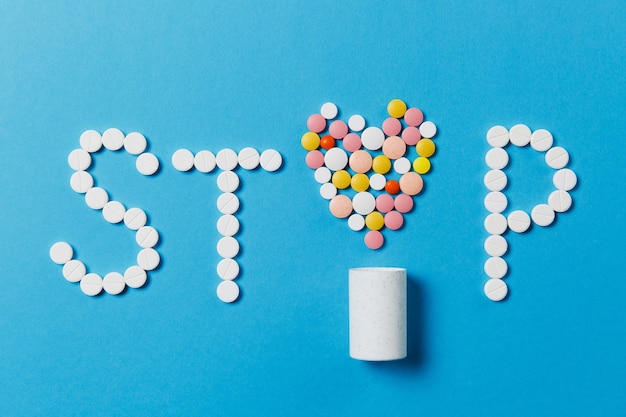 Medication white, colorful round tablets in word Stop isolated on blue background