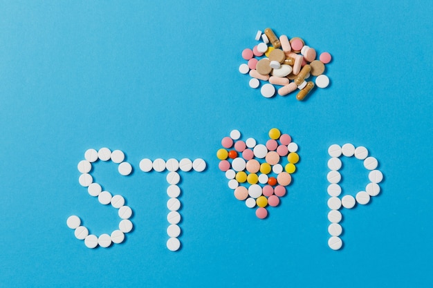 Medication white, colorful round tablets in word Stop isolated on blue background