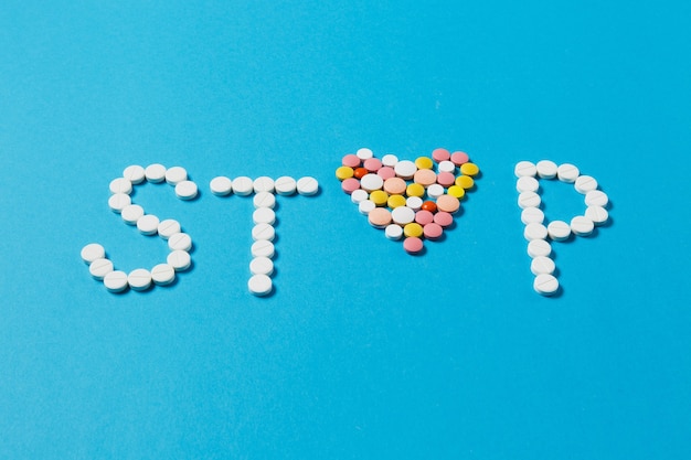 Medication white, colorful round tablets in word Stop isolated on blue background