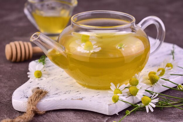 Medicinal chamomile tea with honey in a transparent teapot on a wooden background