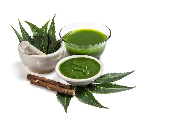 Medicinal Neem leaves in mortar and pestle with neem paste, juice and twigs on white background