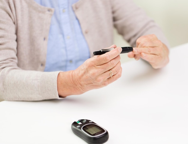 medicine, age, diabetes, health care and people concept - close up of senior woman with glucometer checking blood sugar level at home