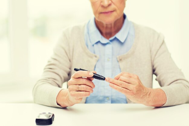 medicine, age, diabetes, health care and people concept - close up of senior woman with glucometer checking blood sugar level at home