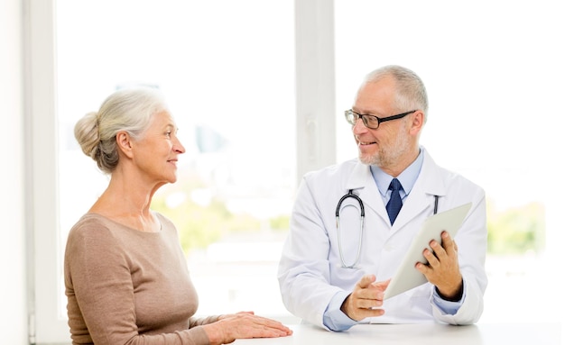 medicine, age, health care and people concept - smiling senior woman and doctor with tablet pc computer meeting in medical office