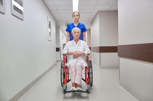 medicine, age, support, health care and people concept - nurse taking senior woman patient in wheelchair at hospital corridor