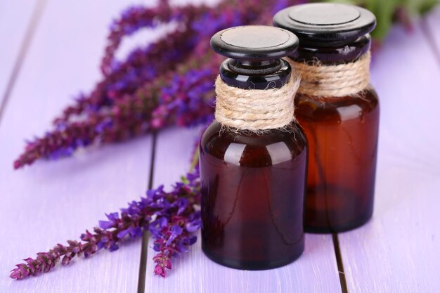 Medicine bottles and salvia flowers on purple wooden background