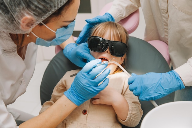 Medicine, dentistry and healthcare concept. a dentist with a dental drill and a saliva ejector treats a child's teeth in a dental clinic