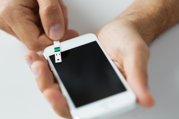 medicine, diabetes, glycemia, health care and people concept - close up of man with smartphone and test stripe checking blood sugar level at home