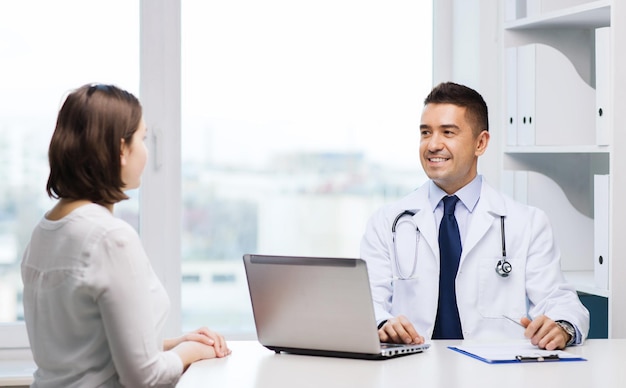 medicine, health care and people concept - smiling doctor with laptop computer and young woman meeting at hospital