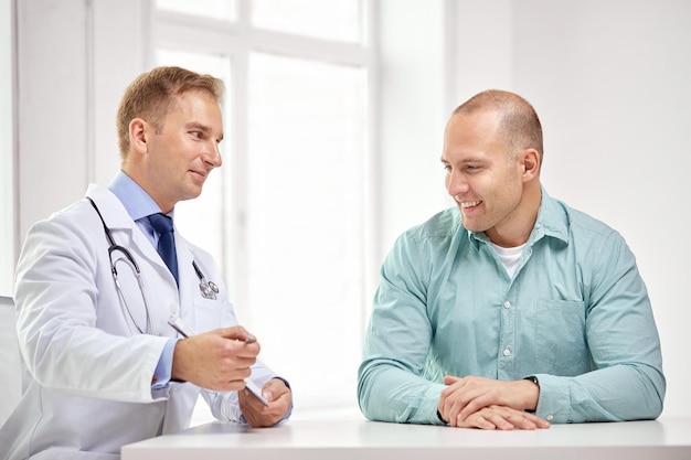 medicine, health care, people and prostate cancer concept - happy male doctor with clipboard and patient meeting and talking at hospital