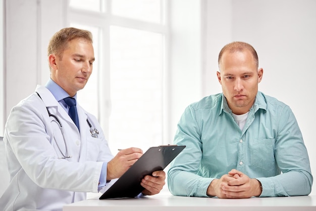 medicine, health care, people and prostate cancer concept - male doctor with clipboard and patient meeting and talking at hospital