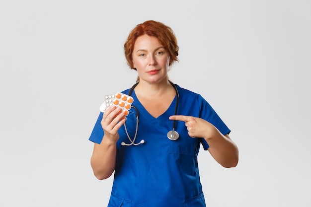 Medicine, healthcare   concept. Confident professional medical worker, female doctor in scrubs prescribe treatment, pointing finger at tablets, pills or vitamins