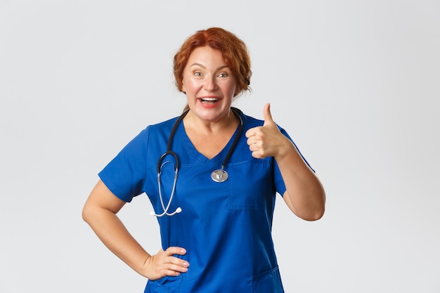 Medicine, healthcare   concept. Upbeat redhead middle-aged doctor  showing thumbs-up and smiling, approve choice