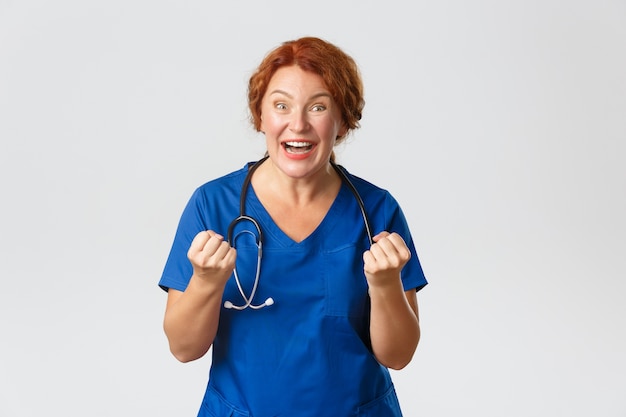 Medicine, healthcare and coronavirus concept. Excited middle-aged doctor, female medical worker fist pump and saying yes with happy smile, winning, celebrating achievement, successful operation.