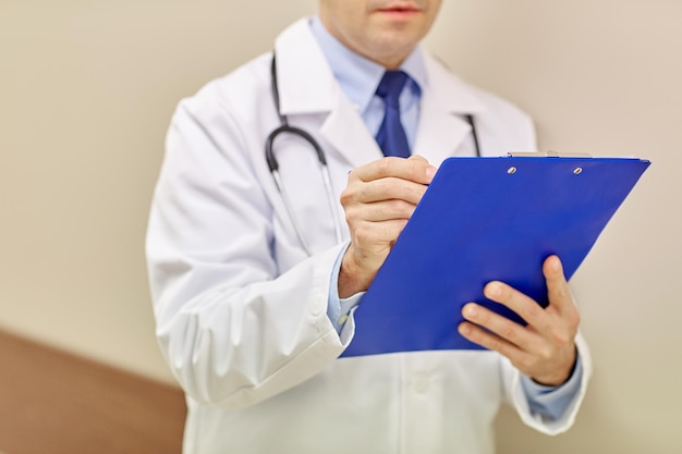 medicine, healthcare, profession and people concept - close up of male doctor with clipboard at hospital