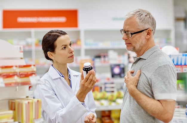 medicine, pharmaceutics, health care and people concept - pharmacist showing drug to senior man customer at drugstore