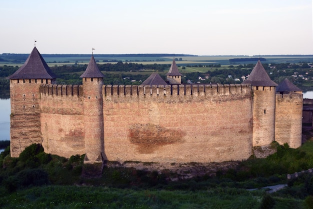 Medieval stone fortress with several crenellated towers And behind it distant meadows and forests