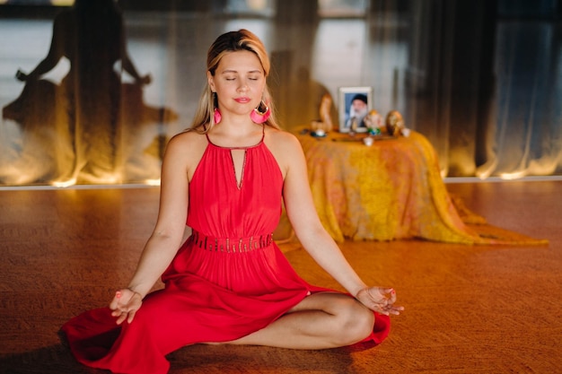 Meditation and concentration a woman in a red dress sitting on the floor with her eyes closed is practicing medicine indoors Peace and relaxation