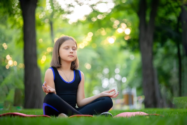 Meditation in the park in the lotus position little girl meditates and relaxes