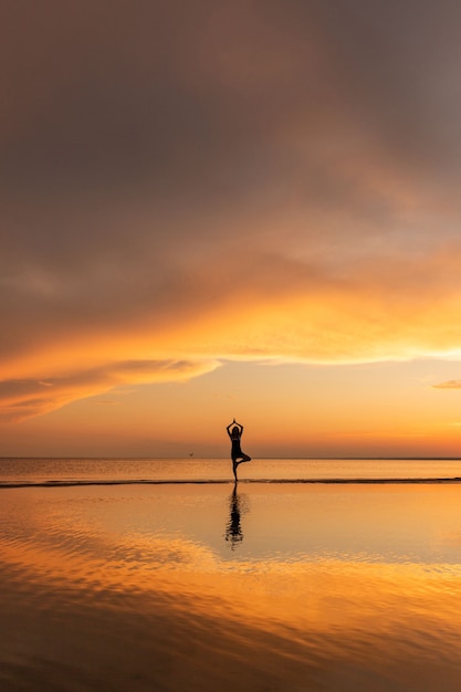 Meditation woman practicing tree yoga pose on the beach at sunset