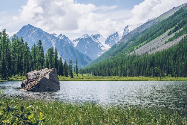 Meditative view to beautiful lake with stone in valley on snowy mountains background.