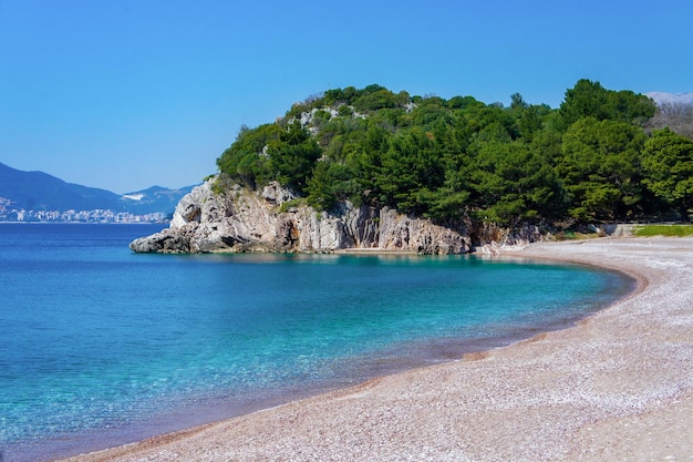 Mediterranean blue sea beach with small orange pebbles rocks with green pine trees