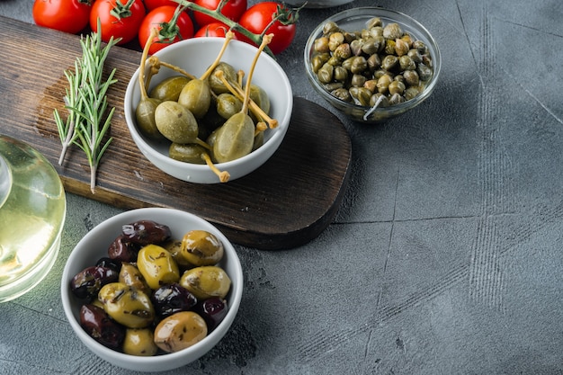 Mediterranean olives and capers with herbs, on gray  