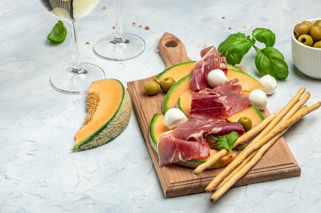 Photo mediterranean salad with prosciutto or jamon mozzarella and green basil leaves and cantaloupe melon on white table traditional spanish and italian appetizer served with wholemeal grissini top view