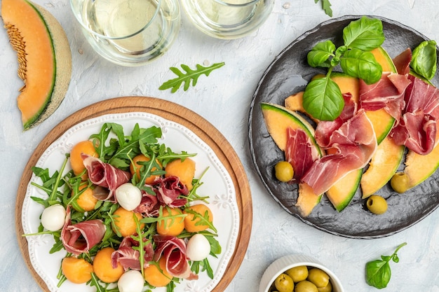 Mediterranean salad with prosciutto or jamon mozzarella and green basil leaves and Cantaloupe melon on white table traditional Spanish and Italian appetizer served with wholemeal grissini top view