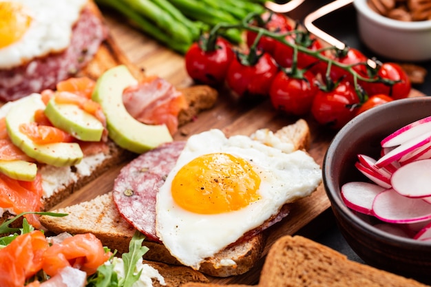 Mediterranean snacks set with brushettas, cheese variety, salami, eggs and salmon over black on wood board, top view